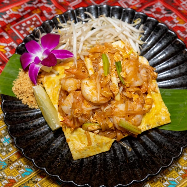 Shrimp Pad Thai wrapped in an egg crepe, garnished with bean sprouts, lime, and an orchid.