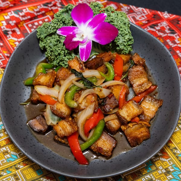 Crispy pork belly stir-fry with onions, bell peppers, and basil, garnished with kale and an orchid.