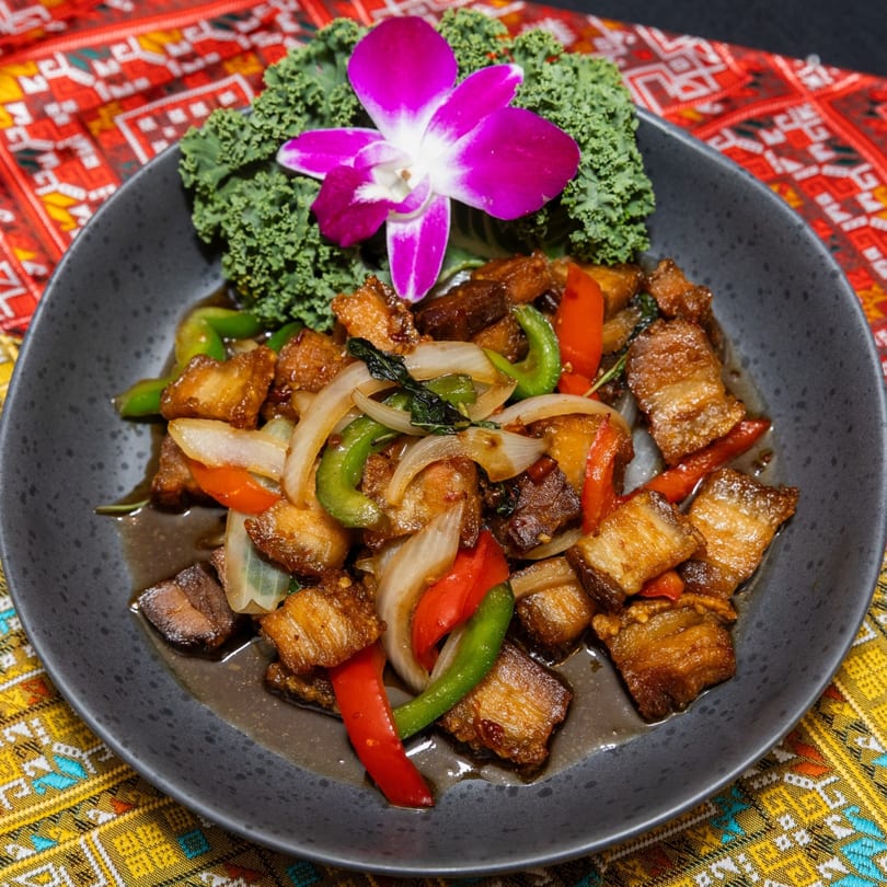 Crispy pork belly stir-fry with onions, bell peppers, and basil, garnished with kale and an orchid.