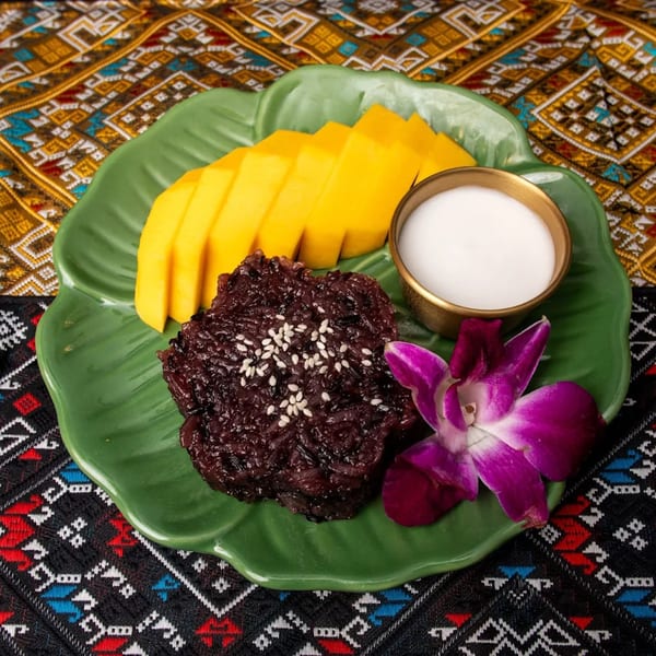 Mango sticky rice with black glutinous rice, coconut milk, and an orchid on a green plate.