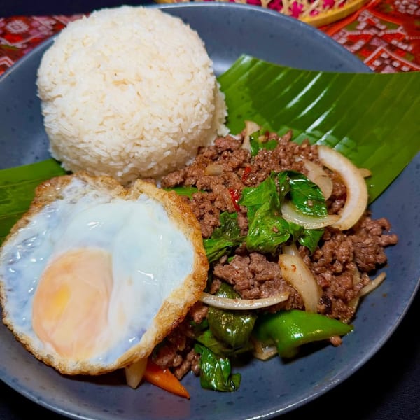 Thai basil beef with white rice and a fried egg on a banana leaf-lined plate.