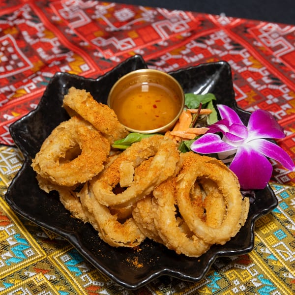 Crispy fried calamari rings with a sweet chili dipping sauce, salad, and purple orchid on a black plate.