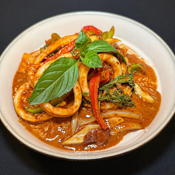 Spicy Thai red curry with squid, bell peppers, onions, and basil on a white plate.